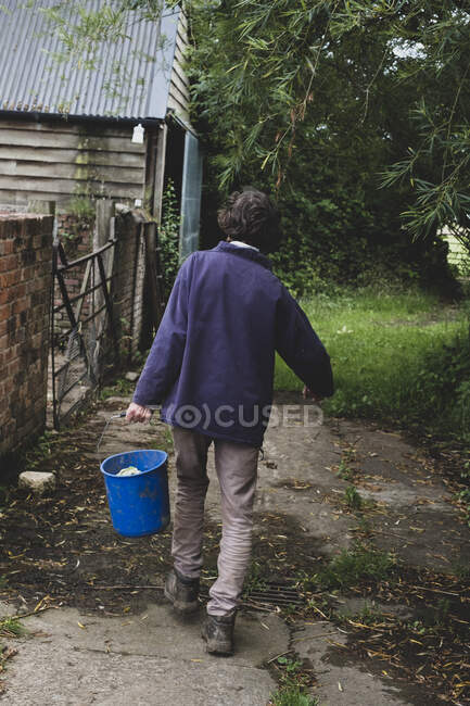 Vista trasera de la mujer en una granja, llevando cubo de plástico azul. - foto de stock