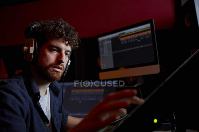 Человек, работающий в музыкальной студии с помощью компьютера в наушниках — стоковое фото
