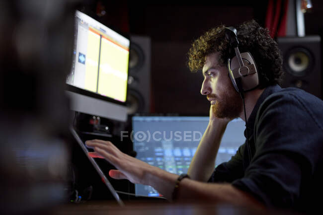 Hombre trabajando en un estudio de música usando un ordenador con auriculares - foto de stock