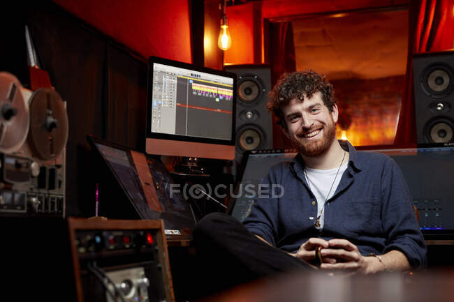 Retrato del hombre sonriendo a la cámara sentado en el estudio de música sosteniendo una taza de café - foto de stock