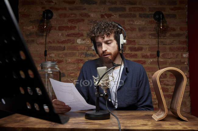 Retrato del hombre usando auriculares en el estudio sosteniendo un pedazo de papel hablando en el micrófono - foto de stock