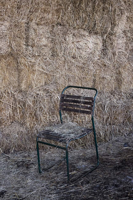 Black metal chair in front of wall of hay bales. — Photo de stock