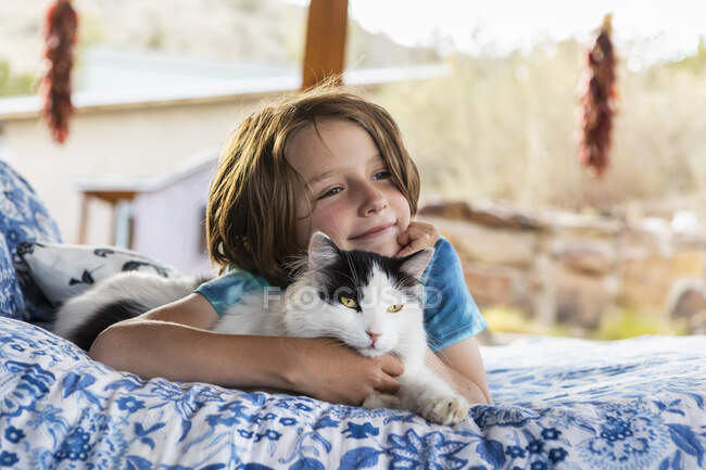 Мальчик лежит на открытой кровати обнимая кота — стоковое фото