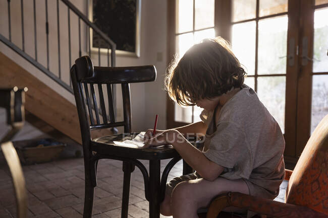 Young boy writing on small chair at sunset — Stock Photo