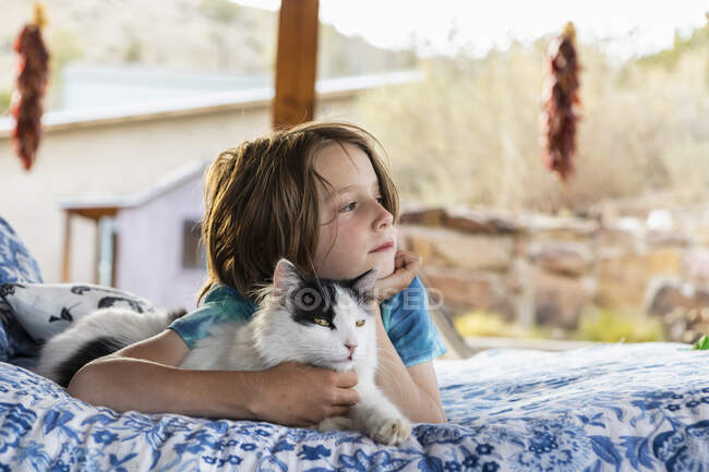 Young boy lying on outdoor bed embracing cat — Fotografia de Stock