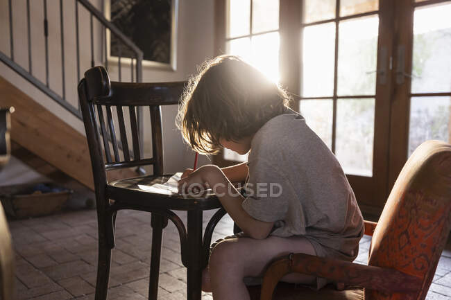 Молодий хлопчик пише на маленькому стільці на заході сонця — стокове фото