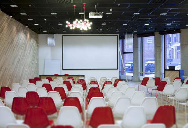 Large empty room with red and white chairs in rows, ready for a presentation — Foto stock