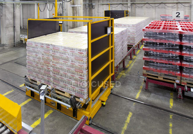 Warehouse and distribution centre for goods, pallets, lifting equipment and racking. Shrink wrapped cartons and boxes of beer for transport. Rolling bench — Photo de stock