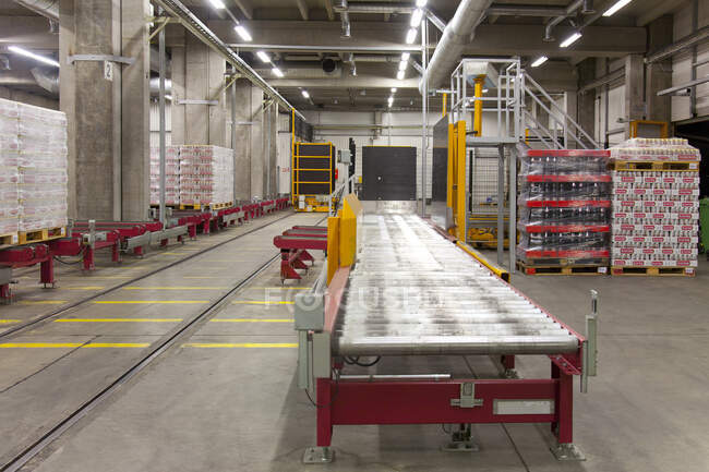 Warehouse and distribution centre for goods, pallets, lifting equipment and racking. Shrink wrapped cartons and boxes of beer for transport. Rolling bench — Photo de stock