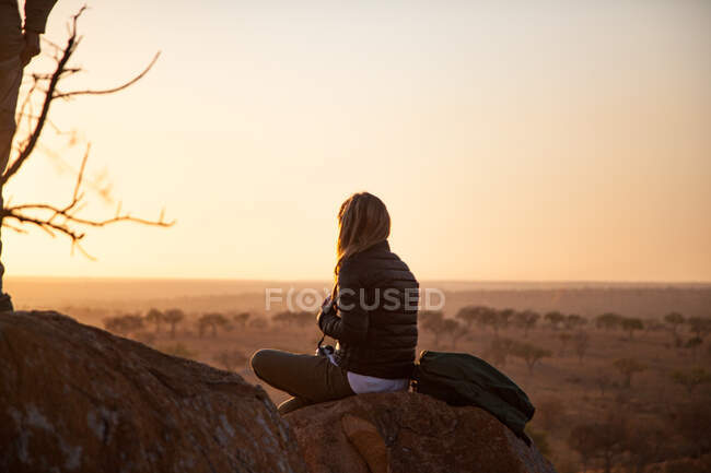 Eine Frau sitzt auf einem Felsbrocken und beobachtet den Sonnenaufgang — Stockfoto