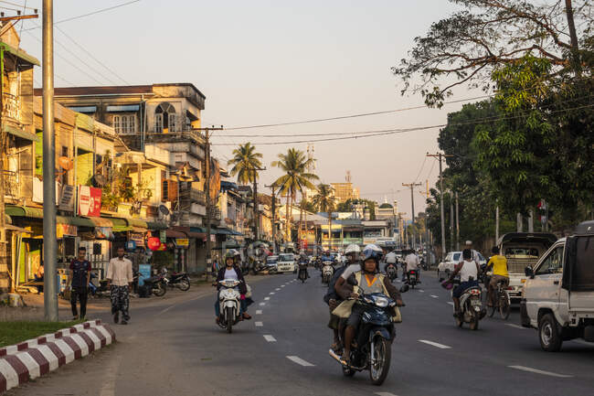 Mawlamyine, Ladenfronten und Straßenverkehr bei Sonnenuntergang, Motorräder und Fußgänger. — Stockfoto