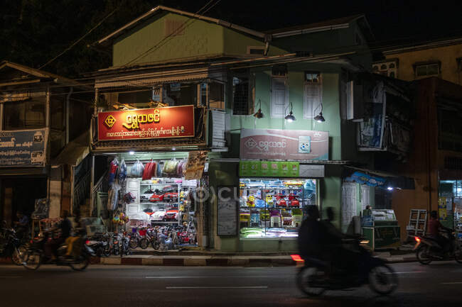 Mawlamyine, frentes de tiendas y motocicletas en la carretera por la noche - foto de stock
