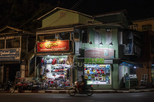 Mawlamyine, frentes de tiendas y motocicletas en la carretera por la noche - foto de stock
