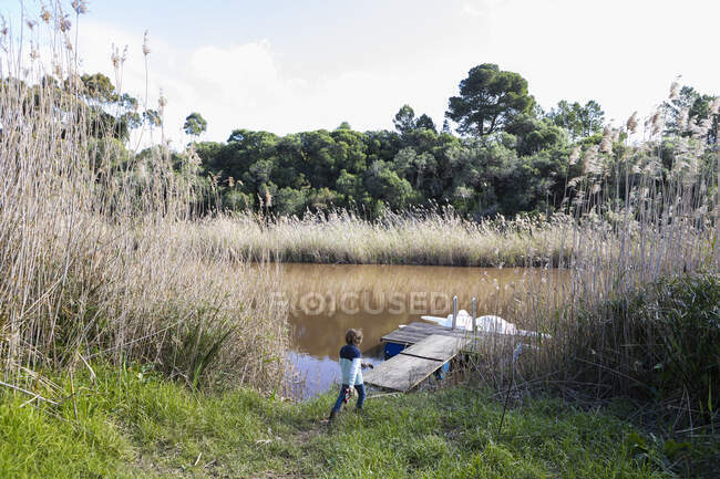 Young boy playing near a lagoon on the Klein River estuary, boat moored at a dock — Stock Photo