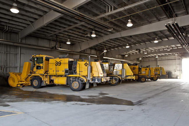Arados de nieve y vehículos del aeropuerto estacionados en un gran cobertizo. - foto de stock