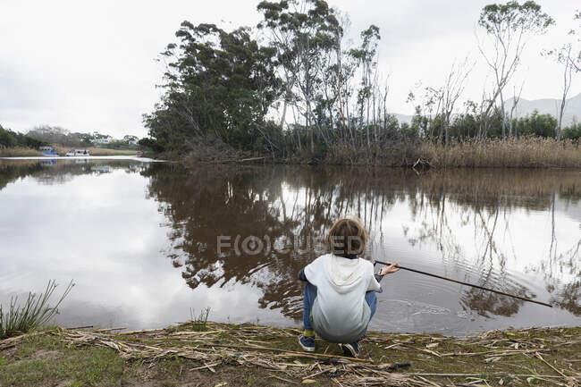 Giovane ragazzo seduto su una riva del fiume — Foto stock