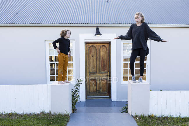 Брат і сестра стоять на низькій стіні біля будинку, сміючись — стокове фото