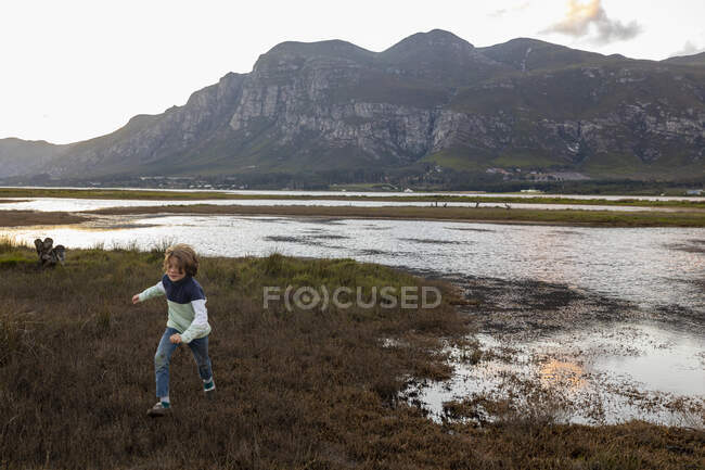 A boy exploring the shore of a lagoon in the shadow of the Klein river mountain range — Stock Photo