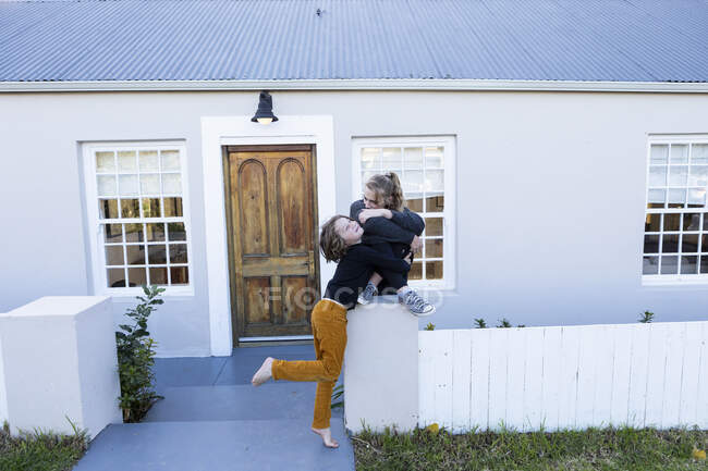 Fratello e sorella fuori dalla loro casa, che si solleticano a vicenda — Foto stock