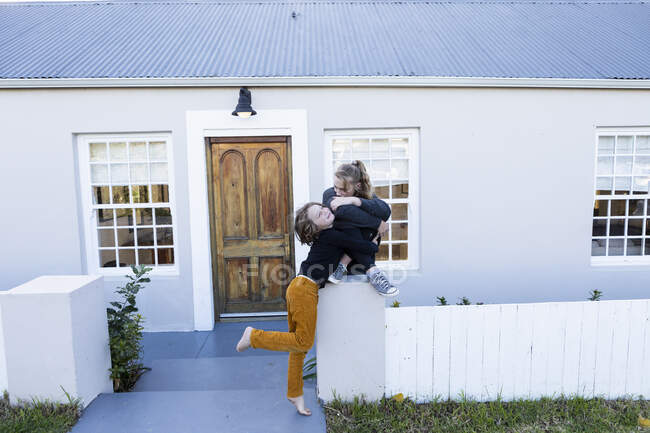 Fratello e sorella fuori dalla loro casa, che si solleticano a vicenda — Foto stock