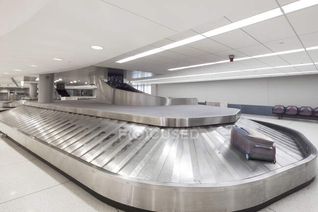 Area di ritiro bagagli dell'aeroporto vuota, una singola borsa su una giostra. — Foto stock