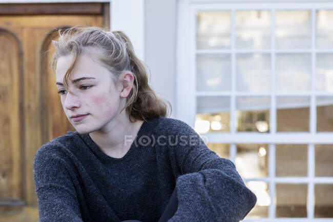 Девочка-подросток, сидящая снаружи одна, выглядит скучающей. — стоковое фото