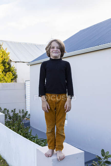 8-річний хлопчик стоїть на стіні біля будинку, позує на камеру . — стокове фото
