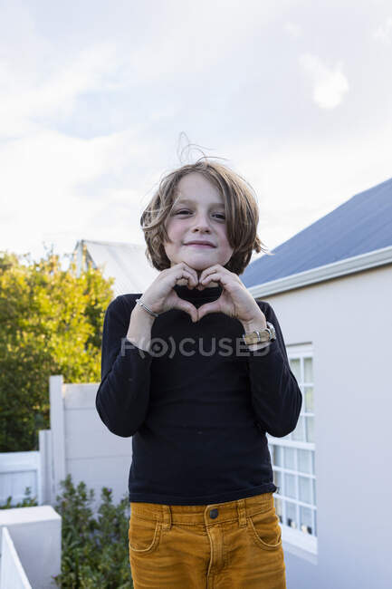 An 8 year old boy standing on a wall outside a house, posing for the camera. — Stock Photo