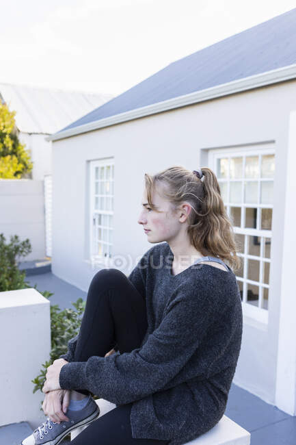 Adolescente sentada fora de uma casa em uma parede baixa, esperando — Fotografia de Stock