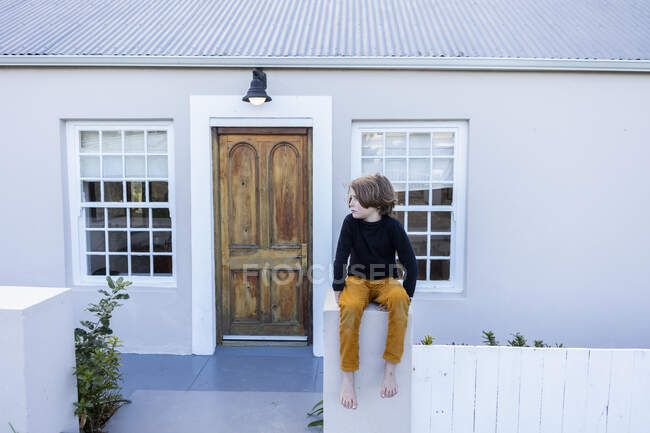 Jeune garçon assis sur un mur à l'extérieur de sa maison — Photo de stock