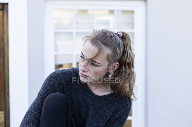 Una adolescente sentada fuera de una casa, sola - foto de stock