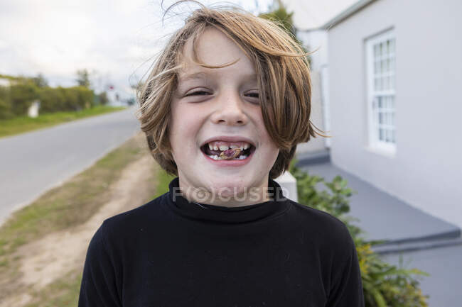 Niño de ocho años con una nuez entre los dientes, una sonrisa dentada - foto de stock