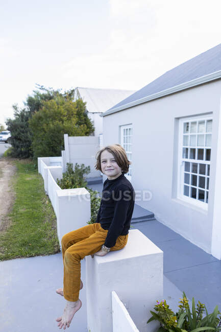 Jeune garçon assis sur un mur à l'extérieur de sa maison — Photo de stock