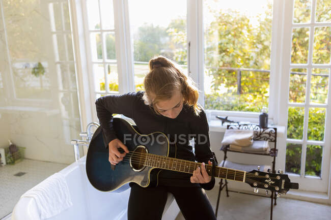 Дівчина-підліток сидить на краю ванни, граючи на губній гітарі . — стокове фото