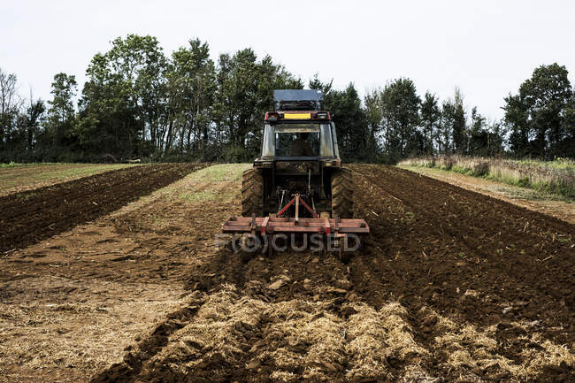 Rückansicht eines Traktors, der ein Feld auf einem Bauernhof pflügt. — Stockfoto