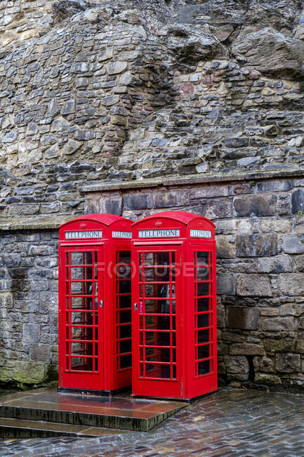Red telephone boxes in front of ancient stone wall. — Stock Photo