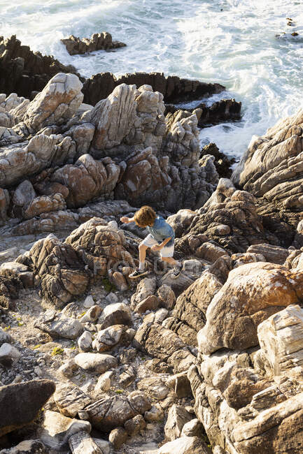 Ein Junge springt über Felsen an der Küste, die Brandung bricht unter. — Stockfoto
