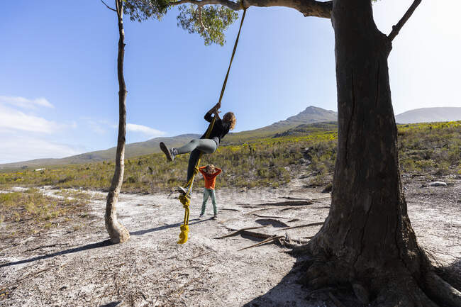 Ragazza adolescente e fratello minore utilizzando altalena corda su un sentiero escursionistico — Foto stock