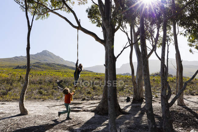Дівчина-підліток і молодший брат використовують мотузкові гойдалки на пішохідній стежці — стокове фото