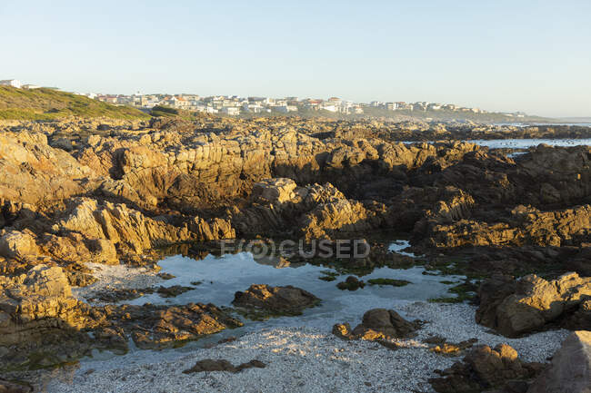 Jagged rocks and rock pools on the Atlantic Ocean coastline and houses on the headland. — Stock Photo