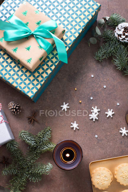 Christmas, top view of gifts, mince pies on a plate and star shapes and lit candles. — Stock Photo