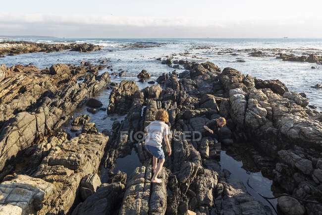 Jovem rapaz escalando e explorando as rochas e piscinas, De Kelders, Western Cape, África do Sul. — Fotografia de Stock
