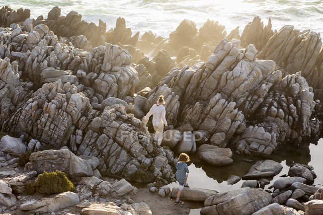 Blick von oben auf ein Teenager-Mädchen, das bei Sonnenuntergang an einem Strand Felspfützen erkundet, De Kelders, Western Cape, Südafrika. — Stockfoto