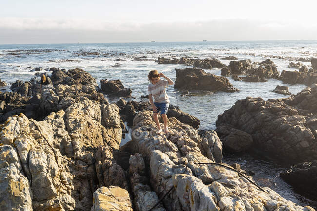 Jeune garçon escaladant et explorant les rochers et les piscines, De Kelders, Western Cape, Afrique du Sud. — Photo de stock