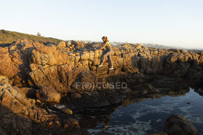 Девочка-подросток поднимается по скалам над каменистым бассейном на побережье Де Келдерс. — стоковое фото