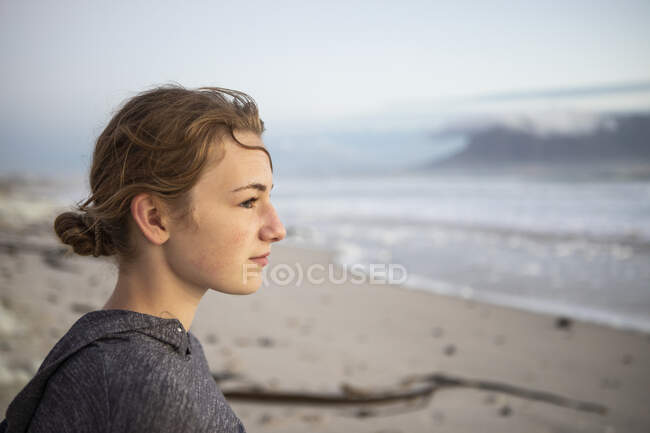 Профіль дівчини-підлітка, яка дивиться в море з пляжу на заході сонця . — стокове фото