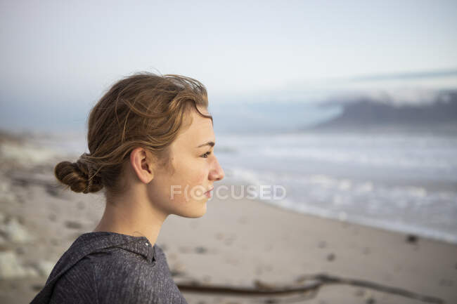 Profil portrait d'une adolescente regardant vers la mer depuis une plage au coucher du soleil. — Photo de stock