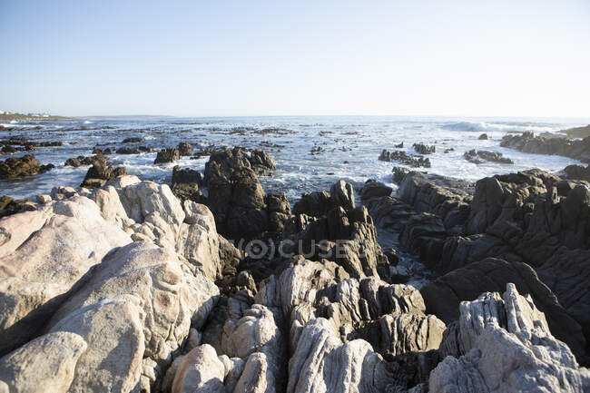 Jagged rocks ridges leading out into the sea, and waves breaking on shore at De Kelders — Stock Photo