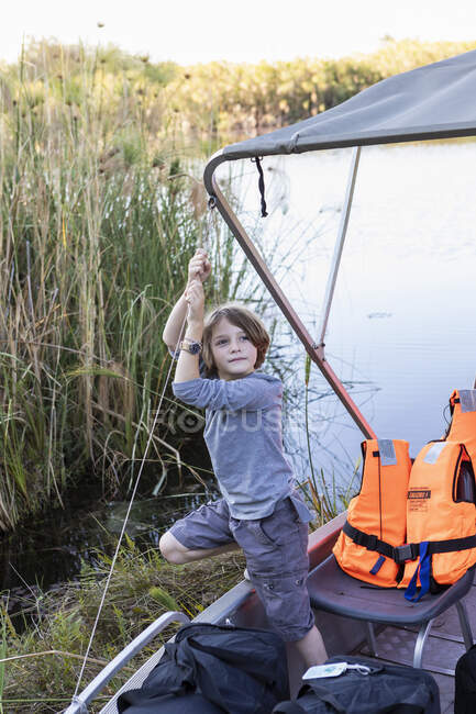 Ein Junge hängt auf dem Baldachin eines kleinen Bootes auf dem Wasser des Okavango-Deltas, Botswana. — Stockfoto