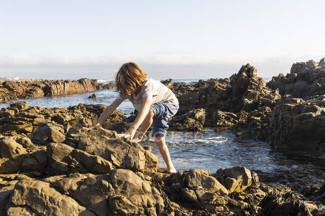 Um jovem garoto explorando as piscinas rochosas em uma costa rochosa do Oceano Atlântico, De Kelders, Western Cape, África do Sul. — Fotografia de Stock